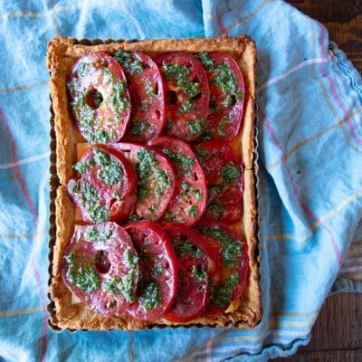 This Tomato Caprese Tart is easy to make with fresh peak season tomatoes, mozzarella cheese, and a pesto - all tucked into a tart shell. Use it for an appetizer, side dish or vegetarian dinner.