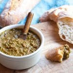 Ramekin of bread dipping oil on a cutting board with slices of French bread.