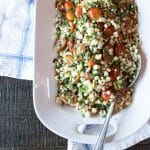 A serving platter filled with a corn and tomato salad with fresh basil and mint.