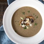 Bowl of puréed mushroom soup topped with sliced mushrooms, scallions and parsley.