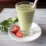 Spinach smoothie with strawberries poured into a glass with a straw.