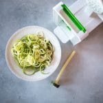 A bowl of spiralized zoodles next to a spiralizer.