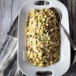 Summer couscous salad with zucchini, summer squash, corn, raisins and pine nuts on a serving platter with a large serving spoon.
