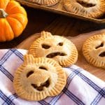 Several apple hand pies in the shape of pumpkins, with carved faces for Halloween.