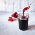 A jar of freshly made pomegranate molasses, with a spoon pour it into the jar.