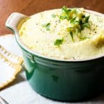 A bowl of cheesy mashed potatoes topped with ground pepper and chopped parsley.