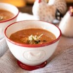A bowl of white bean soup with tomatoes, garnished with Parmesan cheese and parsley.