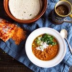 A bowl of curried lentil soup, topped with cilantro, scallions, and sour cream.