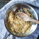 Breadcrumbs browned in a skillet with garlic and lemon zest, with a wooden spoon.