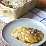 A serving of skinny potato gratin on a small plate, with the remaining gratin in the background.