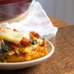 A plate of polenta lasagna with layers of polenta, cheese, sauce and peppers, topped with melted cheese.