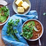 Two bowls of black bean and pumpkin chili topped with slices of avocado, lime and cilantro.