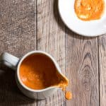 A small pitcher filled with roasted red pepper aioli, with some smeared on a white plate.