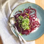 A plate of spiralized beets to look like a beet spaghetti noodles, on whipped feta, topped with micro greens.