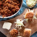 A skillet of sloppy joes, a dish of coleslaw, and a few sliders being made.
