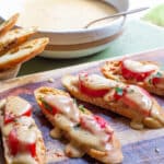 A serving board with crostini stacked with tomatoes, and drizzled with Welsh rarebit cheese sauce.