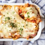 Baked spaghetti casserole topped with melted mozzarella cheese and chopped parsley, with a spoon lifting out a piece.