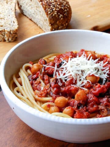A bowl of spaghetti topped with a tomato sauce, chickpeas and Parmesan cheese.