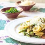 A plate of asparagus carbonara with orcchiette pasta, with Parmesan and parsley in the background.