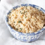 A bowl of cooked, fluffy brown rice topped with a little fresh thyme.