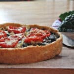 A cauliflower and kale tart with a cheddar cheese crust, topped with roasted tomatoes and cheese.