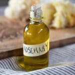 A small bottle of rosemary olive oil, with some bread in the background.