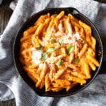 A skillet of roasted red pepper pasta topped with Parmesan cheese and basil leaves.