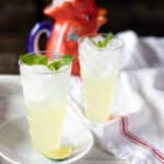 Two tall glasses filled with ice and mojitos, topped with mint leaves.