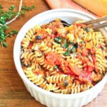 A serving bowl of Sicilian pasta dish of fusilli tossed with eggplant, tomatoes and capers.