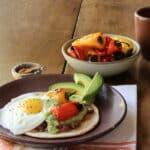 Huevos Rancheros on a plate with roasted mini peppers in a bowl beside it.