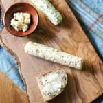 Two logs of compound butters on a cutting board with some spread on a slice of bread.