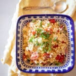 A blue bowl filled with simple corn and tomato salad topped with slivers of basil.