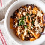 Roasted butternut squash and red onions tossed with dates, chickpeas, and a tahini sauce in a serving bowl.