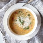 A bowl of creamy white bean soup topped with parmesan cheese and sprigs of rosemary.